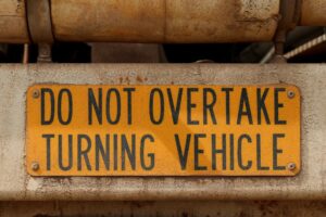 A truck displaying a warning sign with yellow and black colors indicating "Do Not Overtake Turning Vehicle" on its rear.