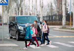 School children wearing medical masks cross the road. They are on their way to school. 