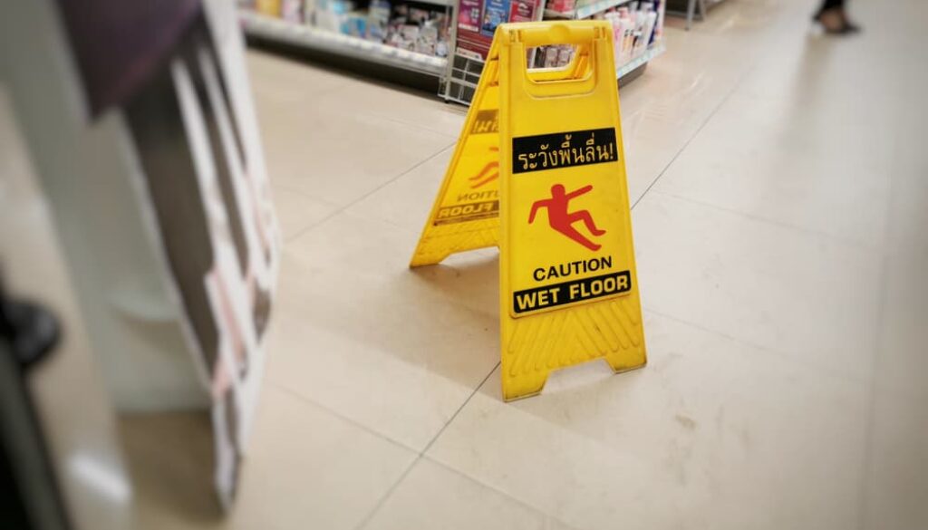 A yellow sign warning of a wet floor is displayed in the supermarket, with blurry products in the background.