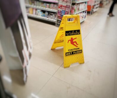 A yellow sign warning of a wet floor is displayed in the supermarket, with blurry products in the background.