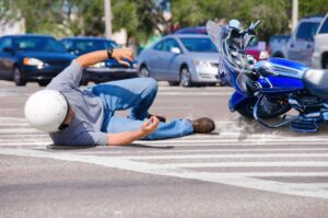 Motorcycle rider wearing a helmet lying on the ground after falling from a blue motorcycle in a crosswalk.