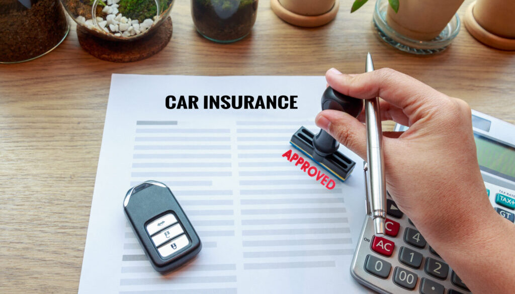 Car insurance document with a car key, calculator, and a hand stamping 'Approved.' Small plants in the background on a wooden desk.
