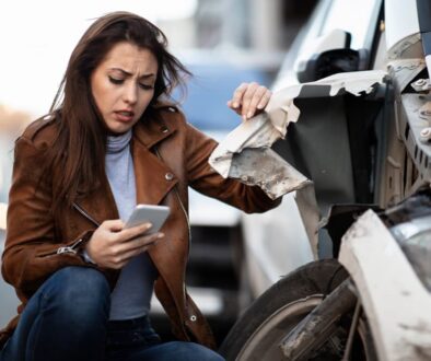 A woman inspecting car damage after a drunk driving accident in Oklahoma, holding her phone to document the scene.