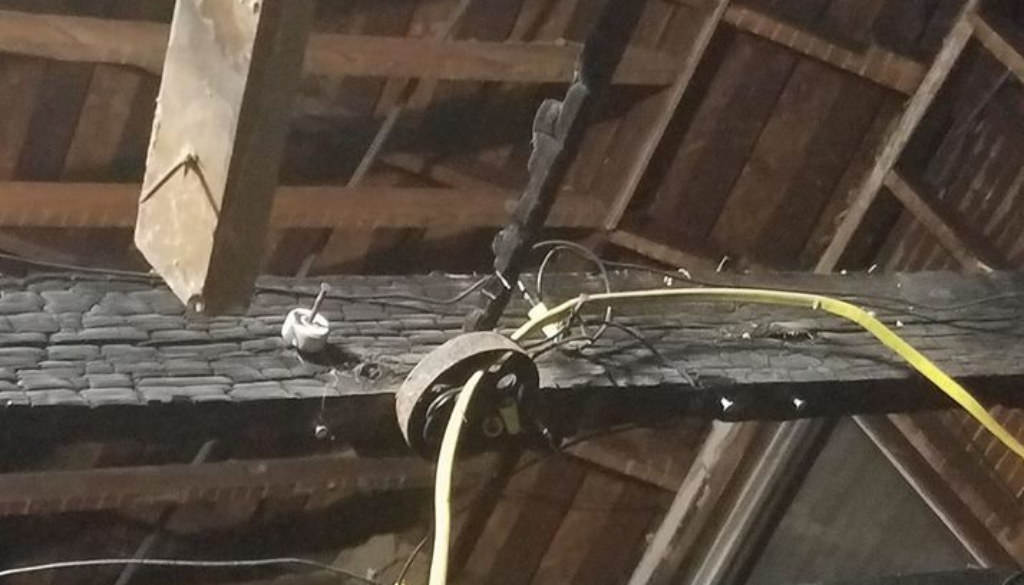 Exposed fire damage in the rafters and beams of a home, showing burnt wood and concealed electrical wiring beneath the surface.