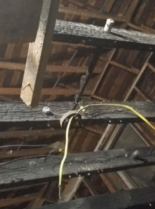 Exposed fire damage in the rafters and beams of a home, showing burnt wood and concealed electrical wiring beneath the surface.