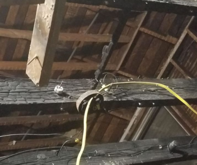 Exposed fire damage in the rafters and beams of a home, showing burnt wood and concealed electrical wiring beneath the surface.