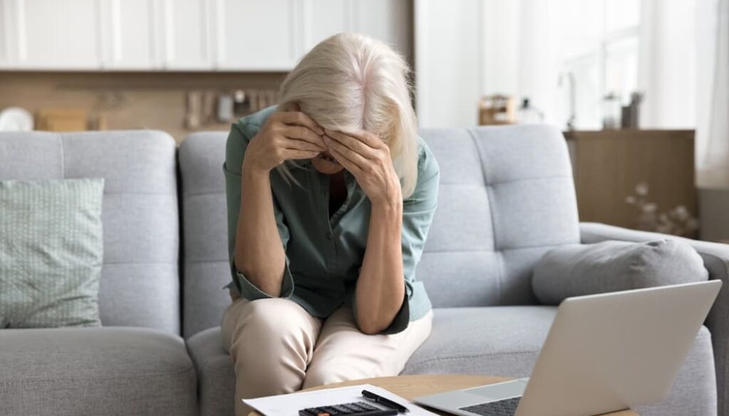 Grieving woman sitting on couch with head in hands, overwhelmed by financial stress after losing a loved one in a car accident.