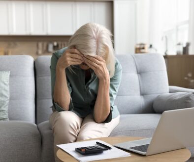 Grieving woman sitting on couch with head in hands, overwhelmed by financial stress after losing a loved one in a car accident.