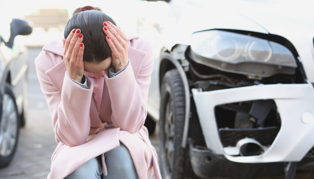 Stressed woman after car accident in Tulsa with vehicle damage, needing Uninsured Motorist Insurance assistance