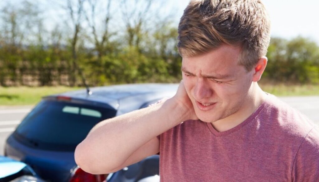 Injured car accident passenger holding his neck beside a vehicle