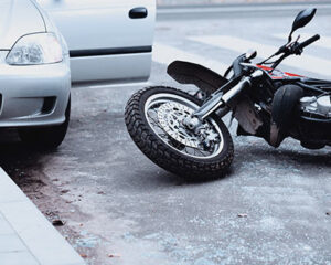 Motorcycle crash scene beside a silver car at a crosswalk