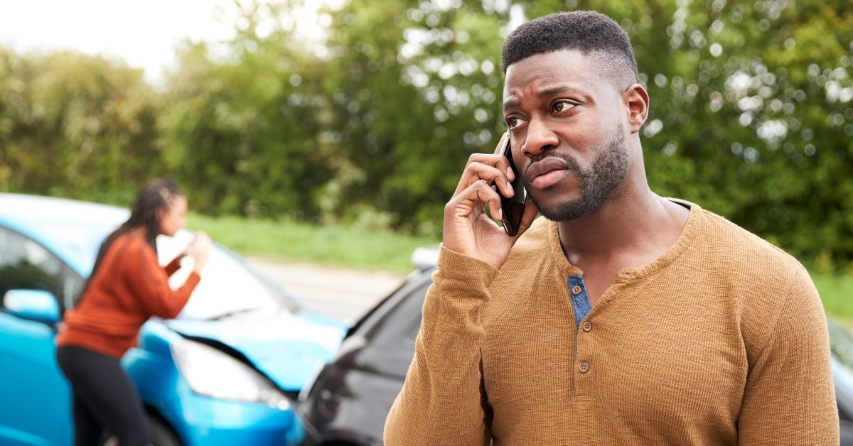 Man on phone after a car crash, with woman inspecting vehicle in background near Tulsa