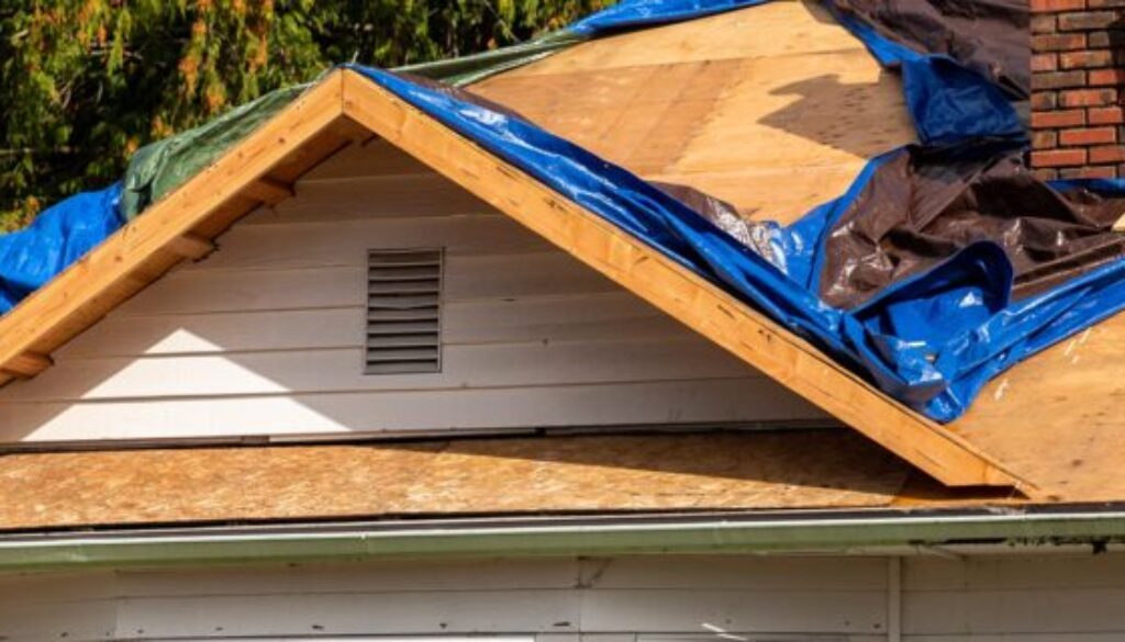 Storm-damaged Oklahoma home with tarped roof and exposed plywood after denied insurance claim”